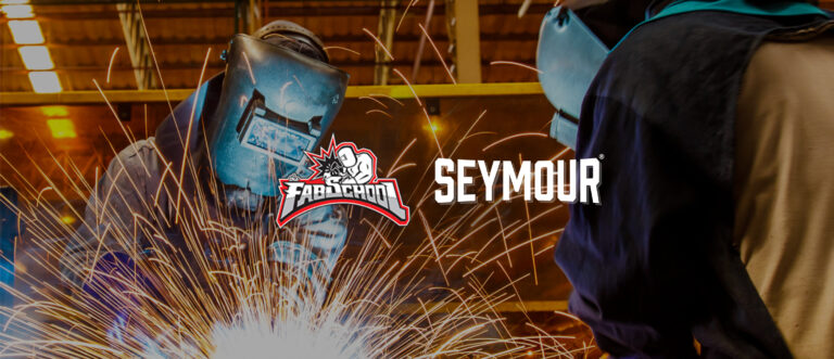 Two welders wearing protective gear work on a metal project, sparks flying around them; the Seymour logo is superimposed on the image.